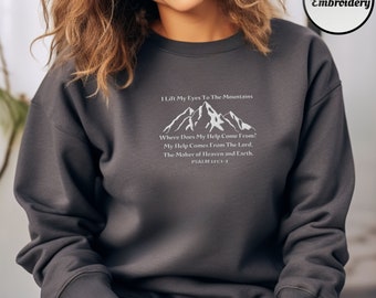 May include: A dark gray sweatshirt with a white mountain graphic and the text "I Lift My Eyes To The Mountains Where Does My Help Come From? My Help Comes From The Lord, The Maker of Heaven and Earth. PSALM 121:1-2"