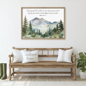 May include: A framed watercolor print of a mountain landscape with pine trees. The print has the text "I lift up my eyes to the mountains... Psalm 121:1-2". The print is displayed above a wooden bench with pillows that say "welcome home".