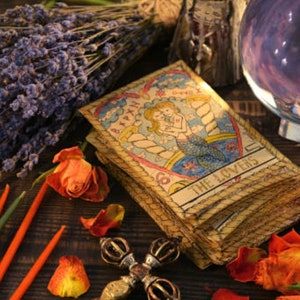 May include: A tarot card reading spread with the Lovers card face up. The card is surrounded by dried lavender, orange roses, and candles. A crystal ball and a crystal are also in the image.