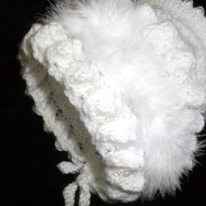 Op de afbeelding: Witte gehaakte baby muts met een witte veren rand en parel accenten.