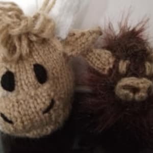 May include: Two knitted animal plushies, one brown and one beige. The beige plush has a smiling face with black eyes and a brown nose. The brown plush has a fuzzy texture and a simple face with black eyes and a brown nose.