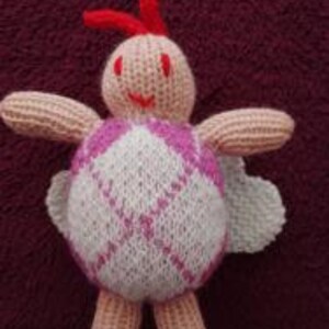 May include: A pink and white knitted turtle with a red antenna and a pink face. The turtle has a checkered pattern on its shell.