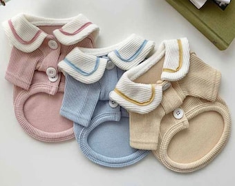May include: Three pet shirts with sailor collars in pink, blue, and beige. Each shirt has a button closure and a white collar with a contrasting colored trim.