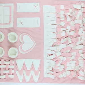 Op de afbeelding: Roze en witte hondenverrijkingsmat met verschillende texturen en vormen, waaronder een hart, een raster en een zigzagpatroon. De mat is ontworpen om honden mentaal te stimuleren en te vermaken.