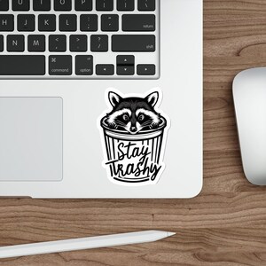 Water resistant feral raccoon trash panda funny die cut sticker with Stay Trashy slogan, perfect for laptops, tumblers, water bottles, journals, and more! Raccoon gifts for animal lovers in their feral era.