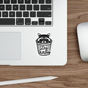 Water resistant feral raccoon trash panda funny die cut sticker with Stay Trashy slogan, perfect for laptops, tumblers, water bottles, journals, and more! Raccoon gifts for animal lovers in their feral era.