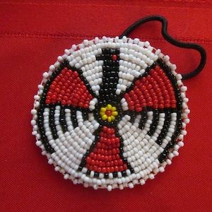 May include: A round beaded hair tie with a black, white, red, and yellow geometric design. The hair tie is made of small beads and has a black elastic band.
