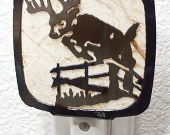 May include: A black metal nightlight with a silhouette of a moose jumping over a fence. The nightlight is plugged into an electrical outlet.
