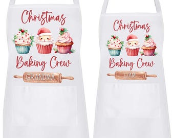 May include: Two white Christmas baking aprons with a red and white Santa Claus and cupcakes design. The aprons have a pocket and a rolling pin with the text "Christmas Baking Crew" and the names "Grandma" and "Liam".