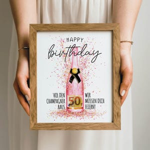 Puede incluir: Impresi&oacute;n enmarcada con marco de madera. La impresi&oacute;n presenta una botella de champ&aacute;n rosa con un lazo negro y el n&uacute;mero 50. Las palabras "Happy Birthday" est&aacute;n escritas encima de la botella, con texto alem&aacute;n debajo.