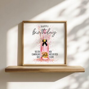 Puede incluir: Impresi&oacute;n enmarcada con marco de madera, con una botella de champ&aacute;n rosa con un lazo negro y las palabras "Happy Birthday" en cursiva. El n&uacute;mero "50" es prominente, con confeti y texto en alem&aacute;n.