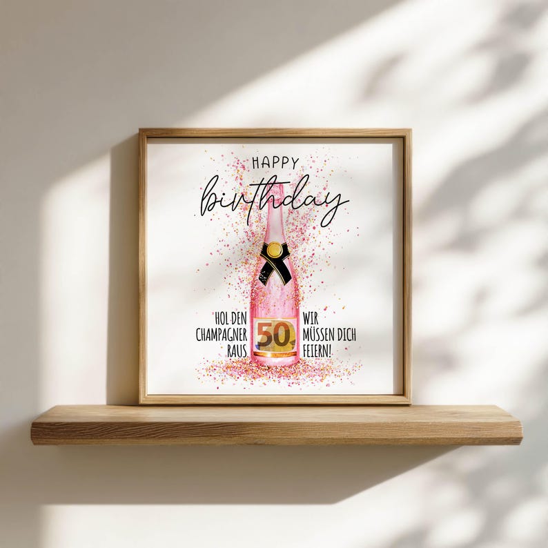 Puede incluir: Impresi&oacute;n enmarcada con marco de madera, con una botella de champ&aacute;n rosa con un lazo negro y las palabras "Happy Birthday" en cursiva. El n&uacute;mero "50" es prominente, con confeti y texto en alem&aacute;n.
