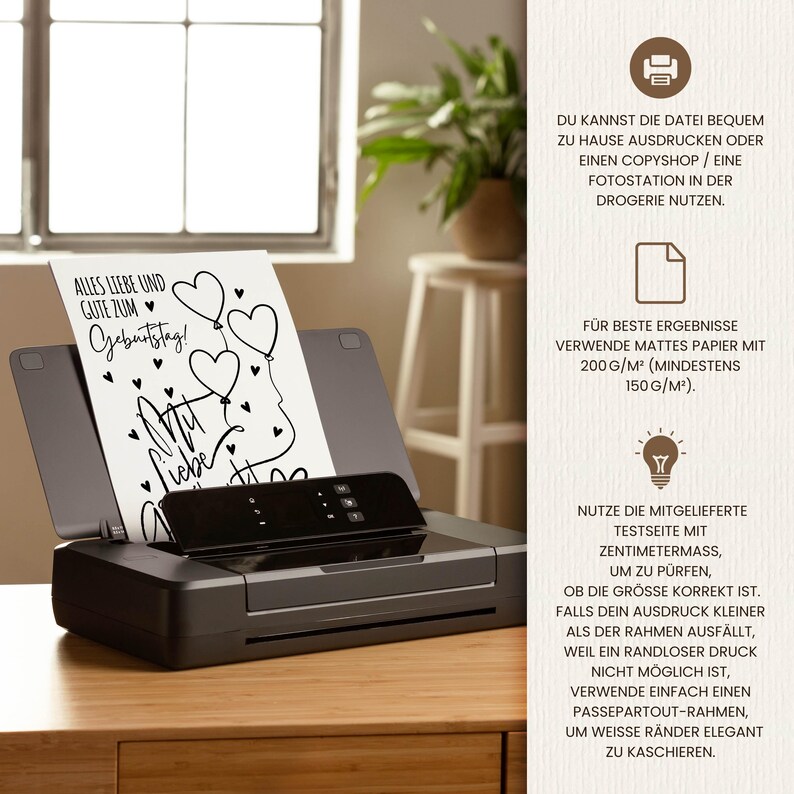 May include: A black printer with a white sheet of paper inside, featuring the text "Alles Liebe und Gute zum Geburtstag!" and heart-shaped balloons. The printer sits on a wooden surface.