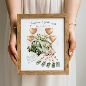 May include: A framed print featuring a green vintage car decorated with flowers and a bow, with heart-shaped balloons. The print includes German text and illustrations of money. The frame is made of wood.