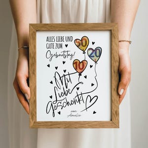 May include: A framed print with a wooden frame, featuring a birthday message in German. The artwork includes heart-shaped balloons with the numbers 10, 20, and 50, along with black heart accents and the words "Alles Liebe und Gute zum Geburtstag!" and "Mit Liebe geschenkt!"