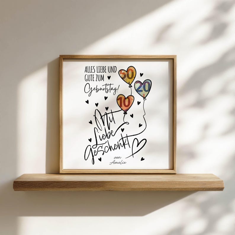May include: A framed print with the text "Alles Liebe und Gute zum Geburtstag!" and "Mit Liebe geschenkt". The print features three colorful balloons with the numbers 10, 20, and 60. Black hearts are scattered around the text and balloons.