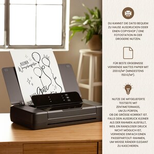 May include: A black inkjet printer with a printed card featuring balloon illustrations and the text "Kleiner Wunschzettel" and "Alles Gute". The printer is on a wooden surface, with a window and a stool in the background.