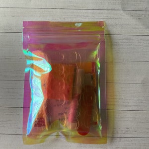 May include: A clear iridescent plastic bag with a zipper closure containing several small, colorful, rectangular items. The items are partially visible through the bag.