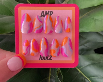 May include: A set of ten pink, orange, and purple swirl-patterned false nails on a pink and orange card with the text "AMP NAILZ".
