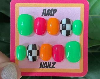 Puede incluir: Un conjunto de seis uñas postizas con un diseño a cuadros, verde, naranja y rosa. Las uñas se muestran en una tarjeta rosa y amarilla con el texto "AMP NAILZ".