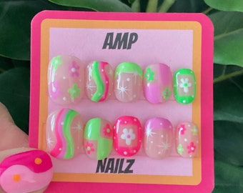 May include: A set of ten pink and green press-on nails with different designs. The nails feature swirls, flowers, and geometric patterns. The card reads "AMP NAILZ".