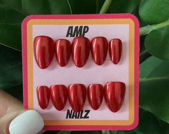 May include: A set of ten red press-on nails with a glossy finish. The nails are arranged in two rows of five on a white card with the text "AMP NAILZ" printed on it.