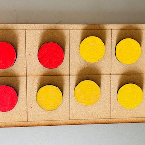 May include: A rectangular wooden ten-frame board featuring two rows of five square slots. The board contains three red circular wooden tokens and seven yellow circular wooden tokens placed within the individual grid sections of the frame.