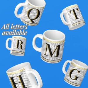 May include: Five white ceramic mugs with black letters and gold trim against a blue background. The letters on the mugs are Q, R, M, H, and G. The text "All letters available" is in the image.
