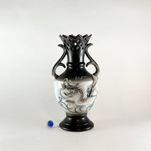 May include: A black and white ceramic vase with a dragon design. The vase has a cut-out design at the top and two handles.