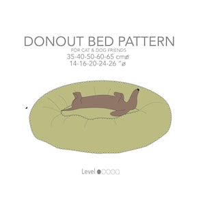 May include: A light green donut-shaped pet bed with a brown dog lying on its back. The bed has a ruffled edge and is labeled "DONOUT BED PATTERN" with size specifications in both centimeters and inches. The text "FOR CAT & DOG FRIENDS" is also included.
