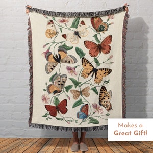 May include: A woven tapestry throw blanket featuring a cream background with a floral design and colorful butterflies. The throw blanket has a fringe border.