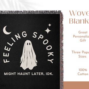 May include: A black woven blanket with fringed edges featuring a white ghost graphic, a crescent moon, and a four-pointed star. The text reads "FEELING SPOOKY" in an arc above the ghost and "MIGHT HAUNT LATER, IDK." in a straight line below.