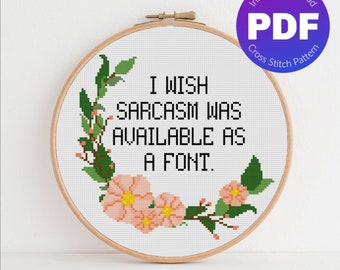 May include: A cross stitch pattern featuring a floral design with pink flowers and green leaves. The text "I wish sarcasm was available as a font." is stitched in black thread.