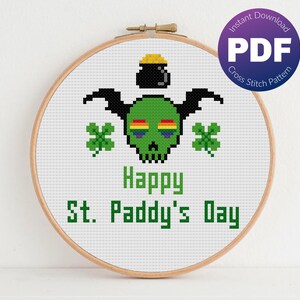 May include: A cross stitch pattern featuring a green skull with rainbow eyes, a pot of gold, and shamrocks. The text "Happy St. Paddy's Day" is below the skull.
