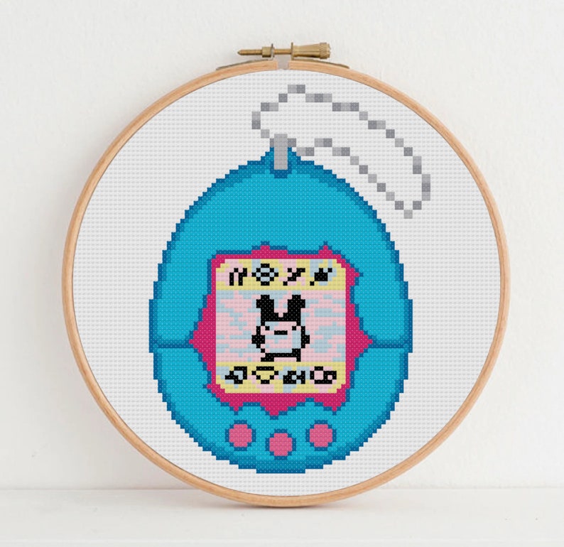 May include: A blue and pink pixelated Tamagotchi keychain with a black and white pixelated bunny on the screen. The screen reads "MOXY".
