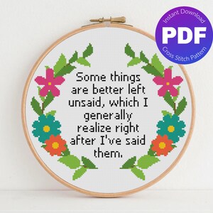 Peut inclure: Un motif de point de croix dans un cercle en bois affiche le texte : « Certaines choses sont mieux non dites, ce que je réalise généralement juste après les avoir dites. » Le motif comprend une couronne florale avec des fleurs roses, turquoise et orange. Un téléchargement PDF est indiqué.