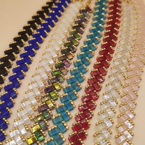 Peut inclure: Gros plan de plusieurs bracelets de perles de différentes couleurs, dont noir, bleu, blanc, irisé, sarcelle, rouge et rose. Chaque bracelet présente un motif tissé avec des accents dorés, créant un affichage texturé et coloré.