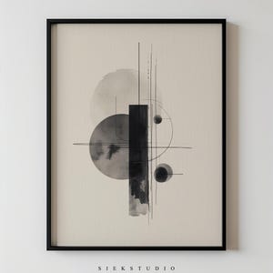 Op de afbeelding: Abstracte kunstprint in een zwarte lijst. Het kunstwerk toont geometrische vormen, waaronder cirkels en rechthoeken, met zwarte en grijze accenten in aquarel-stijl op een beige achtergrond. De tekst "SIEKSTUDIO" staat onderaan.