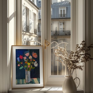 May include: A framed painting of a colorful bouquet of flowers in a blue and white striped vase, set on a windowsill with a view of a Parisian cityscape. Dried flowers in a white pitcher are on the windowsill to the right.