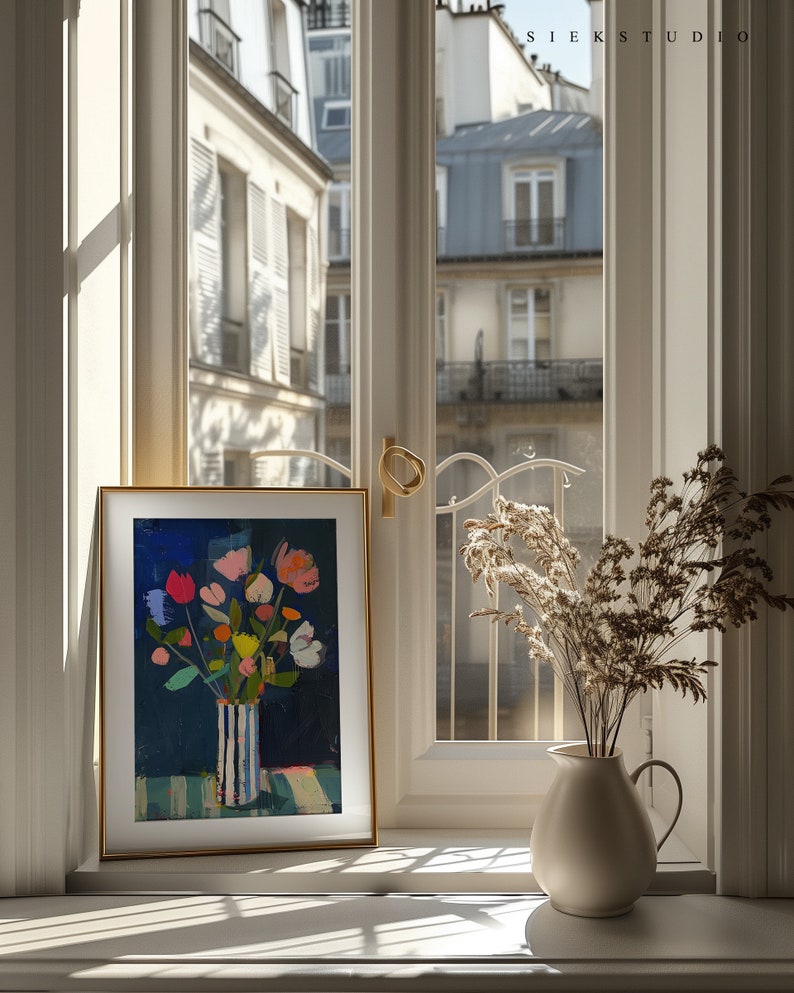 May include: A framed painting of a colorful bouquet of flowers in a blue and white striped vase, set on a windowsill with a view of a Parisian cityscape. Dried flowers in a white pitcher are on the windowsill to the right.