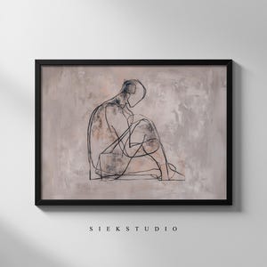 May include: A framed artwork with a minimalist line drawing of a seated person. The black lines contrast against a textured, neutral-toned background. The artwork is encased in a black frame, with the text "SIEK STUDIO" at the bottom.
