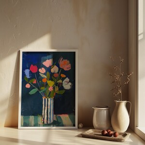 May include: A framed painting of a colorful bouquet of flowers in a striped vase on a blue and white striped background. The painting is set against a white wall with a window and a small plant in the background.