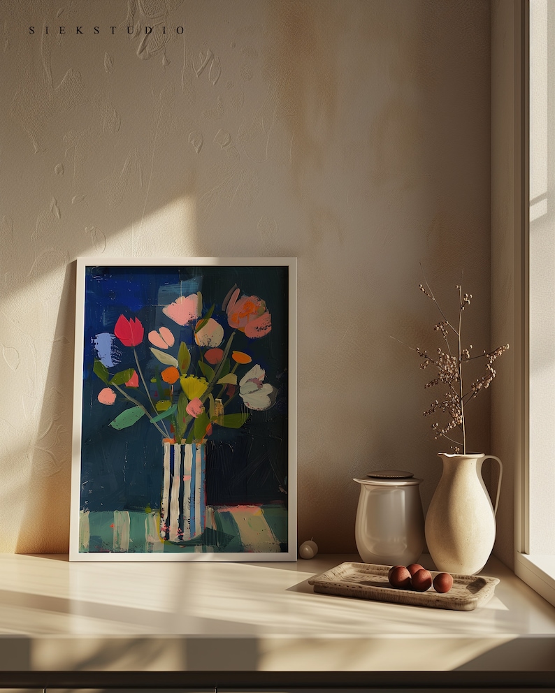 May include: A framed painting of a colorful bouquet of flowers in a striped vase on a blue and white striped background. The painting is set against a white wall with a window and a small plant in the background.