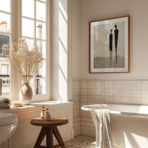 May include: A white bathtub with a towel draped over the edge, a wooden stool with two bottles and a jar on top, and a framed print of two figures on a beige background. The print is titled "SIEKS STUDIO".