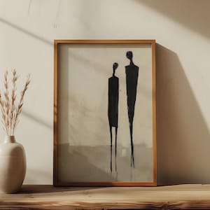 May include: A framed abstract painting of two black figures standing side-by-side on a light beige background. The painting is in a wooden frame and is hanging on a wooden shelf.