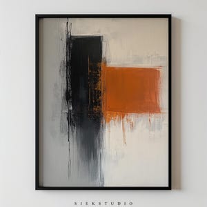 May include: Abstract painting with black, orange, and white paint strokes on a canvas. The painting is framed in a black frame.
