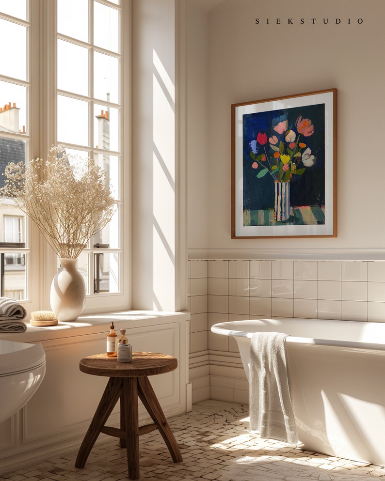 May include: A white bathtub with a white towel hanging over the side, a wooden stool with two bottles and a jar on top, and a framed print of a colorful floral arrangement in a striped vase against a blue background. The print is titled "SIEKSTUDIO".