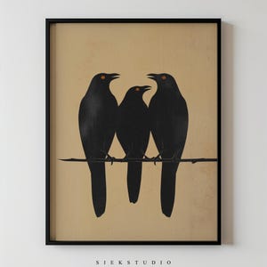 Peut inclure: Impression d'art encadrée représentant trois oiseaux noirs aux yeux orange perchés sur une branche, sur fond beige. L'impression est dans un cadre noir, avec le texte "SIEK STUDIO" en bas. Illustration minimaliste.