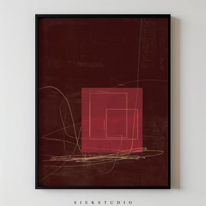 Könnte beinhalten: Gerahmter Kunstdruck mit abstrakter Kunst. Das Kunstwerk hat einen tiefroten Hintergrund mit einem zentralen roten Quadrat, das zwei verschachtelte Quadrate enthält. Feine goldene Linien und der Text "SIEK STUDIO" sind ebenfalls sichtbar.