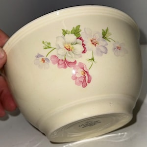 May include: Cream-colored ceramic mixing bowl with a floral design. The bowl features a cluster of white and pink flowers with green leaves. The bowl has a wide rim and a rounded shape, suitable for kitchen use.